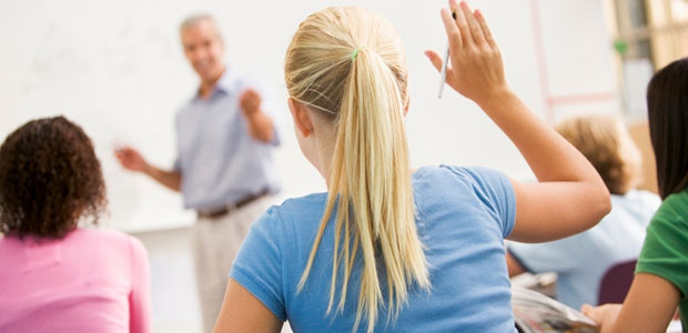 Blonde girl raising hand in class while facing the teacher