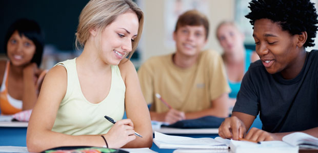 A boy and a girl study together in a classroom with other students in the background