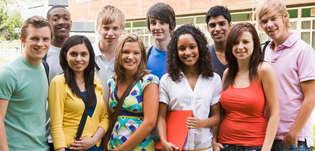 A diverse group of teens stands outside their high school